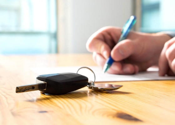 a person signing auto loan documents with keys on a table