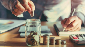 a person putting coins in a glass jar